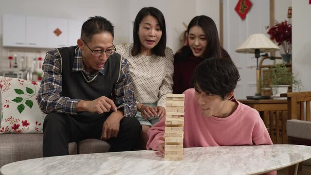 family members and son folding arms and feeling upset as he makes the toy wood blocks tower fall while trying to remove a block. chinese word on door translation: spring