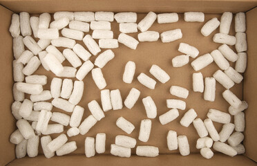 Styrofoam packing peanuts in cardboard box background. White plastic foam pellets protective for parcel packing.