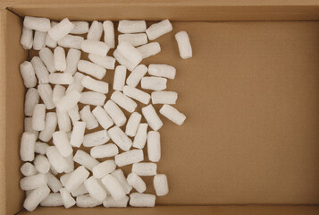 Fototapeta na wymiar Styrofoam packing peanuts in cardboard box background. White plastic foam pellets protective for parcel packing.