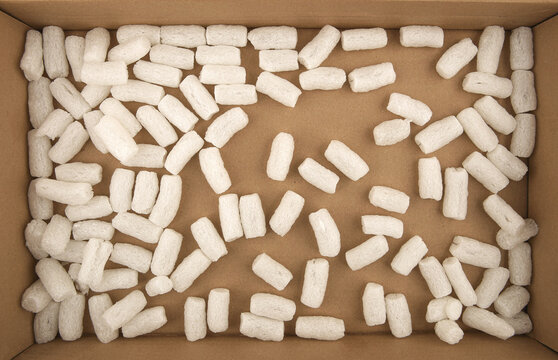 Styrofoam Packing Peanuts In Cardboard Box Background. White Plastic Foam Pellets Protective For Parcel Packing.