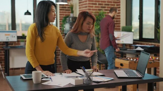 Coworkers doing teamwork on investment project, using information on laptop and financial charts on documents. Company employees working on marketing strategy for development.