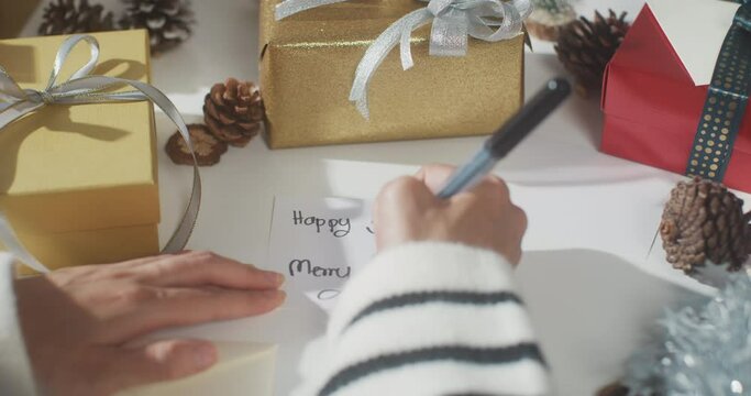 Close up of girl hands writing greeting card winter christmas decorations on table. Minimal creative flat lay of christmas traditional composition and new year holiday season.