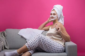 Girl with a cosmetic mask on her face in a white towel. Sits on the sofa.