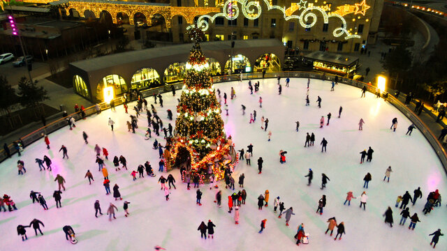 Top View Of People Skate On Ice Rink Around Christmas Tree In Park On Winter Holidays. Active Healthy Lifestyle Entertainment For Family And Kids Outdoor. Ice Skating. Soft Focus