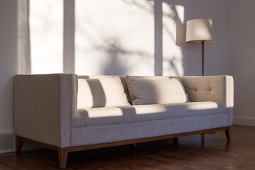 Natural light view of minimalist mid-century style couch and lamp in living room with sun spots and...