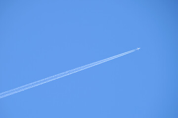 Distant passenger jet plane flying on high altitude on clear blue sky leaving white smoke trace of contrail behind. Air transportation concept