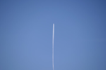 Distant passenger jet plane flying on high altitude on clear blue sky leaving white smoke trace of contrail behind. Air transportation concept