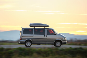 Fototapeta na wymiar Passenger van with roof rack driving fast on intercity road at sunset. Highway traffic in evening