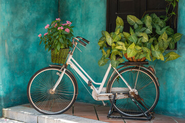 White vintage bike with basket full of flowers next to an old building in Danang, Vietnam, close up