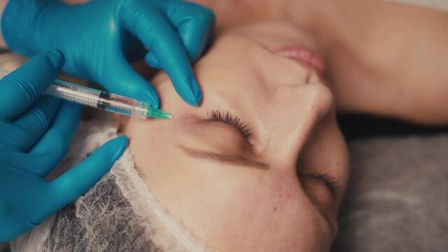 Beauty and injections concept. Experienced beautician entering subcutaneous prick with required active components into female face for tightening and lifting.