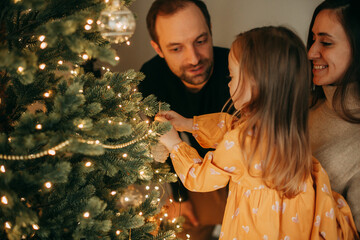 Mom, Dad and Daughter Decorate the Christmas Tree at Home