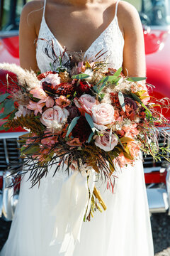 Big extraordinary wedding bouquet in hands of the bride Red vintage car on the background Beautiful modern wedding bouquet in the hands of the bride pink and red color scheme Cropped photo