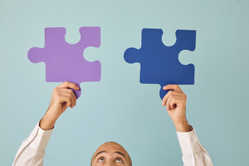 Young guy connecting two perfectly matching puzzle parts. Cropped shot of man looking up at purple...