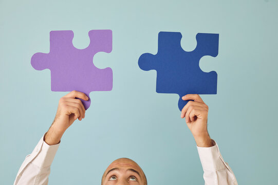 Young Guy Connecting Two Perfectly Matching Puzzle Parts. Cropped Shot Of Man Looking Up At Purple And Blue Paper Jigsaw Pieces He's Holding In Hands. Integration, Education, Finding Solution Concept