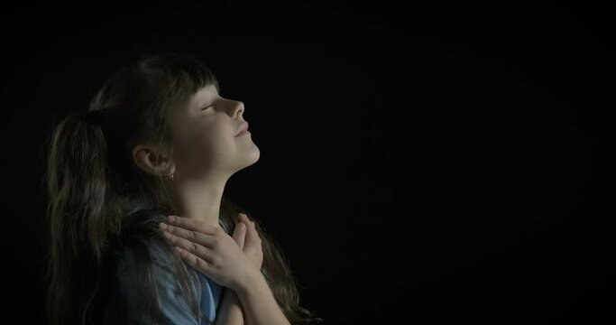 Cute kid is praying. Adorable little girl prays in the dark.