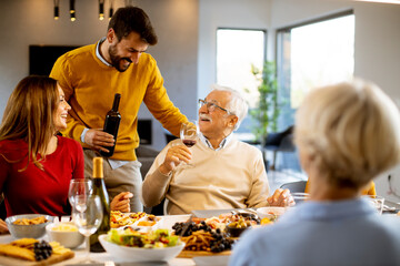 Young man poring red wine to his father for testing during at home