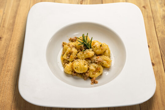 Potato gnocchi seasoned with sausage ragù in a white dish on wooden table