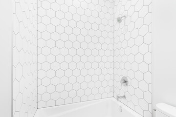 A beautiful white hexagon tiled shower with a white tub and chrome shower head.