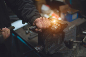 A worker uses a vise and chisel to process hot metal in a workshop.
