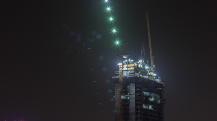 Skyscraper under construction with cranes and iron frame night timelapse
