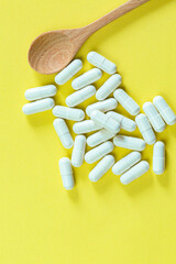 White capsule pills and stacked wood on yellow background