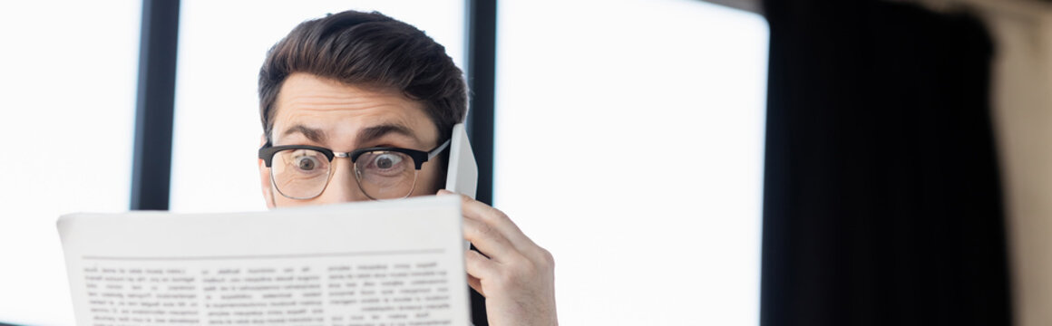 Shocked businessman talking on smartphone while reading news in office, banner.