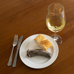 A dish of black pudding accompanied by bread and a glass of white wine