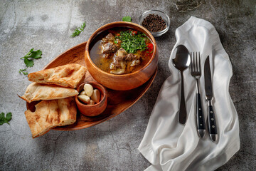 Beef goulage with garlic and pita bread and cutlery on a gray stone table