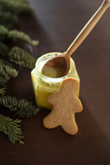 a ginger cookie in the form of a man leans on a jar of honey and a wooden spoon on a wooden table with branches of nobilis on the background. Christmas pastries.