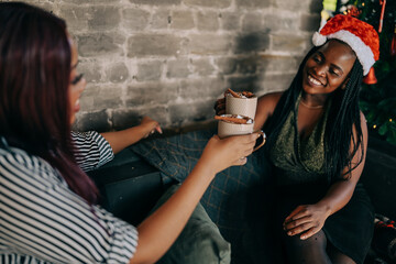Two women celebrating at home winter Christmas holidays near the xmas tree. Indoors lifestile...