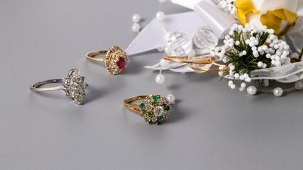 Beautiful gold rings with sparkling diamonds, ruby and emeralds on a gray background. Isolated...