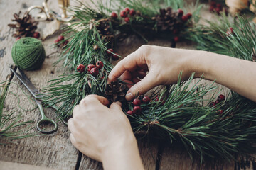 Woman making Christmas wreath by attaching red berries to fir tree branch during Christmas workshop, Handmade advent wreath creation process concept