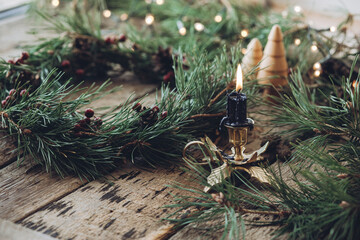 Handmade Christmas wreath with pinecones and red berries on rustic wood table, Countryside advent Christmas celebration with fir garland, candle, and Christmas lights
