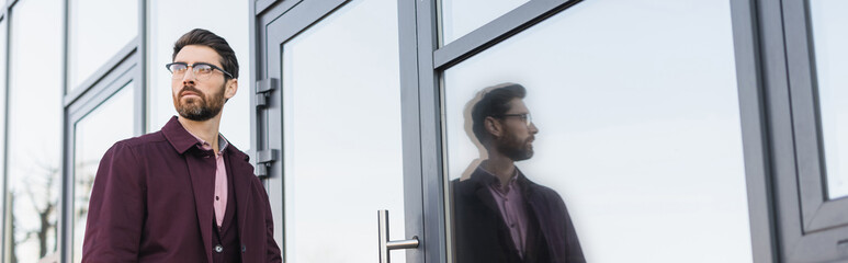 Fototapeta premium Businessman in trench coat walking near building on urban street, banner.