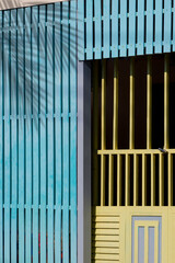 Obraz premium Sunlight and shadow on surface of green steel entrance door in blue wooden lath wall background in vintage style, home renovation concept