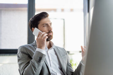 Businessman in formal wear talking on smartphone in office.