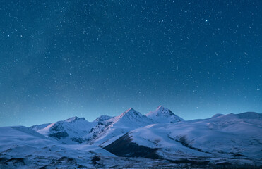 Snow covered mountains under starry sky. Night landscape.