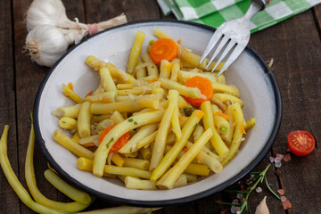 Tin plate with cooked yellow string beans on wooden table. Healthy fat-free and cholesterol-free yellow beans. Vegan food.