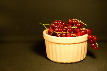 Red currant in a pink bowl on black background close up,summer dessert,image for poster,wall canvas,horizontal cover design,home decor,vegetarian diet,ingredient for cooking,tasty useful snack