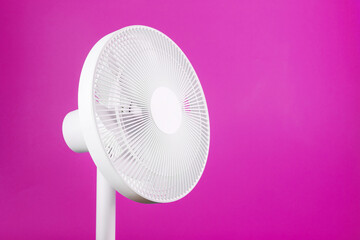 White modern electric fan for cooling the room on a pink background.