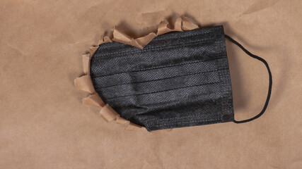 Black medical protective mask on the background of a brown paper heart
