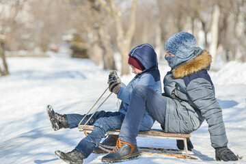 Two boys on sleds go down the snowy hill.