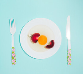 Broken red Christmas bauble decoration with broken egg on sky blue background. Minimal food concept. Happy New Year idea.