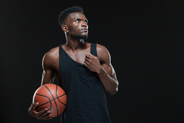 Portrait of afro american male basketball player playing with a ball over black background. Fit...
