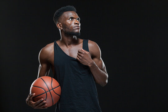 Portrait of afro american male basketball player playing with a ball over black background. Fit young man in sportswear holding basketball