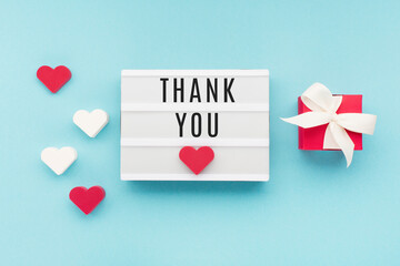 Thank You or thanks greeting card, white lightbox, hearts and red gift box on blue background, top view
