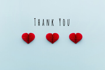 Thank You or thanks greeting card with three red heart on pastel blue background, top view