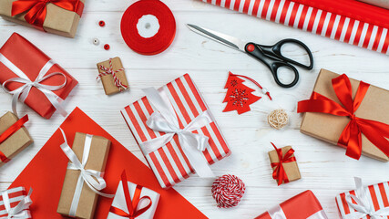 Fototapeta premium Festive composition of decorated presents with christmas tree ornaments, package paper and ribbons on white wooden background