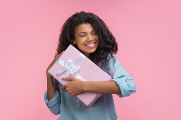 Portrait of young beautiful smiling woman hugging gift box decorated with satin ribbon and showing sincere happiness