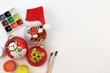 Christmas balls painted with gouache. Tiger symbol of the year 2022 drawn on christmas baubles. Children kids DIY painting hand-made concept. Making christmas tree decoration.